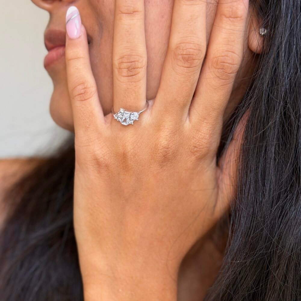 “Sterling silver ring with slightly diagonal rectangular solitaire surrounded by 4–5 small square stones, polished silver band, adjustable, modern geometric design