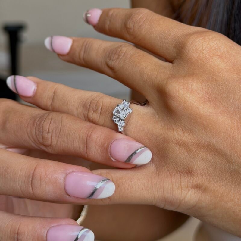 “Sterling silver ring with slightly diagonal rectangular solitaire surrounded by 4–5 small square stones, polished silver band, adjustable, modern geometric design