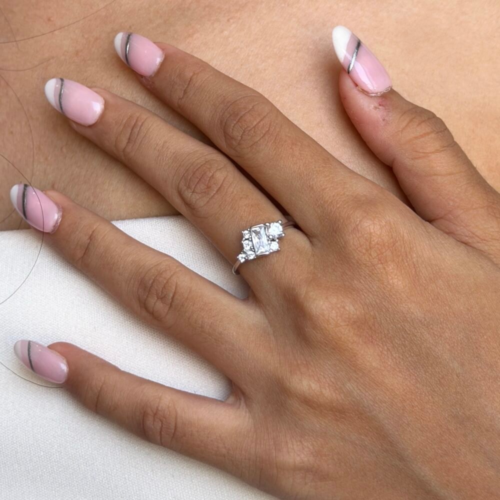 “Sterling silver ring with slightly diagonal rectangular solitaire surrounded by 4–5 small square stones, polished silver band, adjustable, modern geometric design